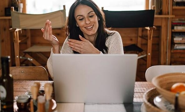 A woman smiling while on a video call with a laptop, representing a live video home tour. Photo by Shixart1985, CC BY 2.0, via Wikimedia Commons
