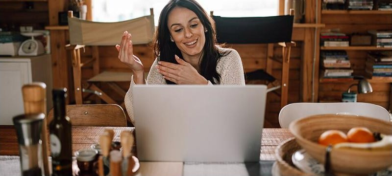 A woman smiling while on a video call with a laptop, representing a live video home tour. Photo by Shixart1985, CC BY 2.0, via Wikimedia Commons