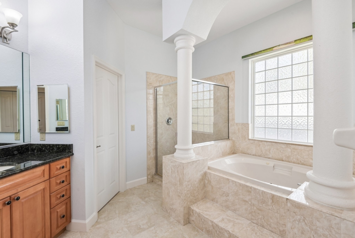 Spa-like primary bath with Jacuzzi tub and separate glass shower in this Seminole FL estate